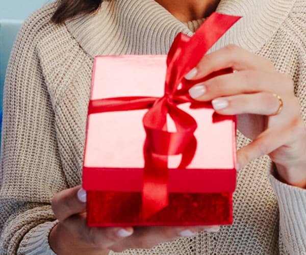 Frau in hellbeigem Strickpullover und passender Mütze hält ihre Hand ans Kinn, blauer Hintergrund