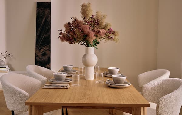 Esszimmer mit Holz-Tisch, gedeckt mit Keramik-Geschirr und Gläsern, Vase mit Blumen, vier gepolsterte Stühle, Kunst an der Wand