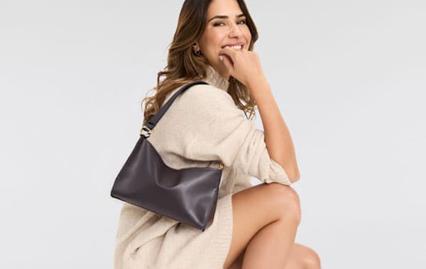 Frau in beige-farbener Kleid, hockend, mit einer schwarzen Handtasche über der Schulter.