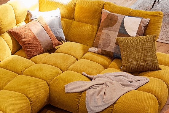 Gelbes Sofa mit mehreren Kissen und einem hellen Kleidungsstück darauf