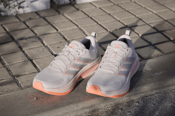 Hellgraue Sportschuhe mit apricotfarbenen Details stehen nebeneinander auf einem gepflasterten Weg