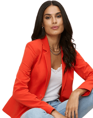 Frau mit langen Haaren trägt leuchtend roten Blazer über weißem Top und hellen Jeans, sitzt lässig