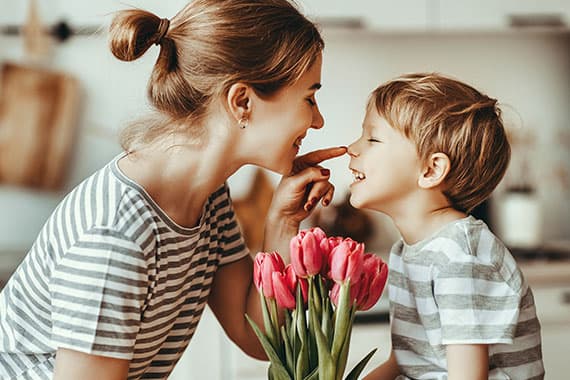 Frau und Kind in gestreiften Shirts beugen sich zueinander, vor ihnen steht ein Strauß rosa Tulpen
