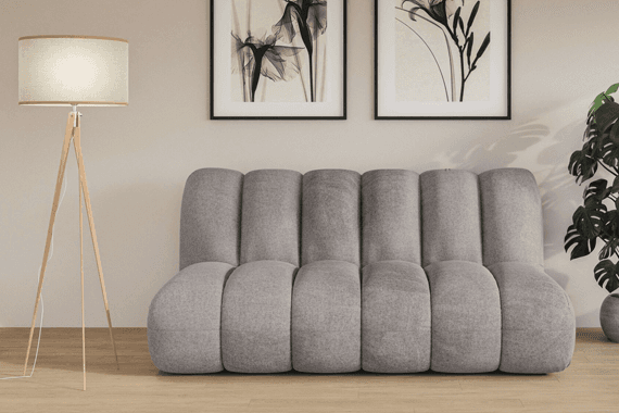 Graues, segmentiertes Sofa vor Wand mit zwei Blumenbildern, links Stehlampe, rechts grüne Zimmerpflanze