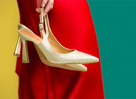 Hand hält beigefarbenen Slingpumps mit Blockabsatz vor rotem Kleid und gelb-grünem Hintergrund