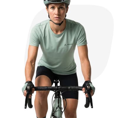 Person mit Helm auf Rennrad, trägt kurzärmliges Trikot und Radhose vor rosa Hintergrundform